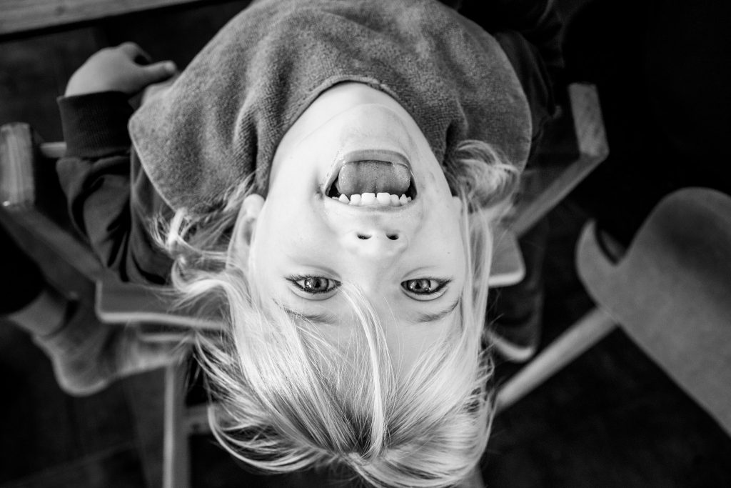 Ein kleines Mädchen mit einem Latz um den Hals kippt ihren Kopf weiter nach hinten und grinst in die Kamera.