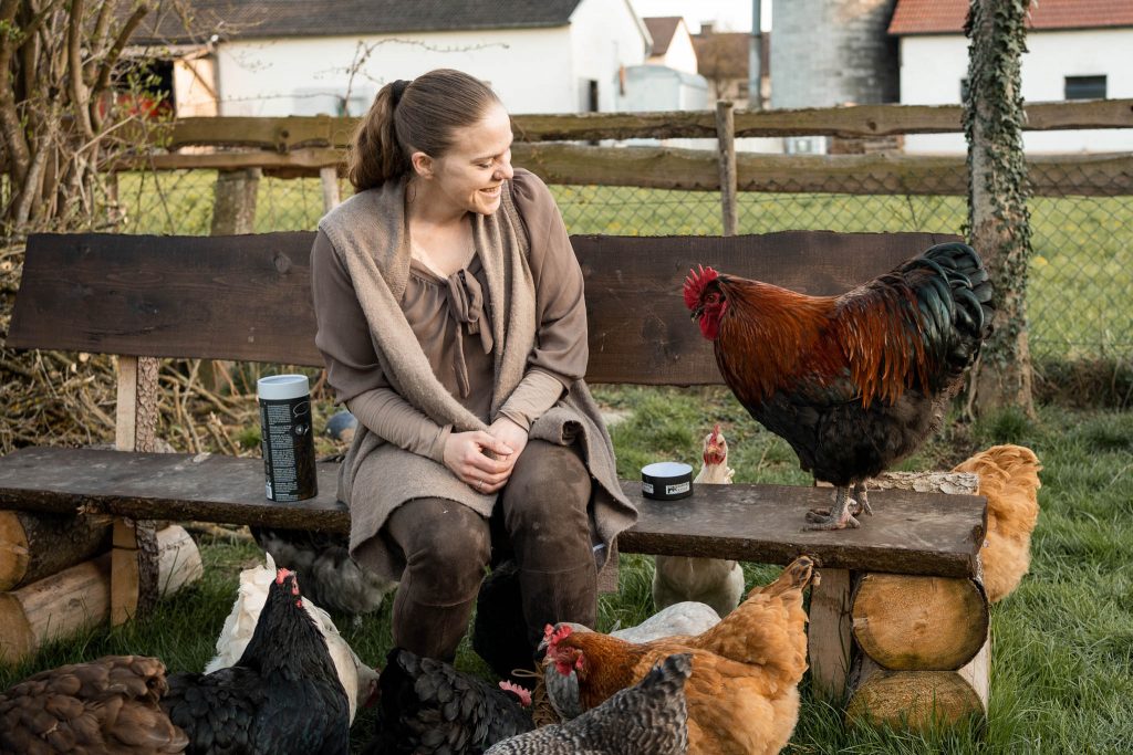 Eine Frau sitzt auf einer Bank in ihrem Garten und erfreut sich an ihren Hühnern.
