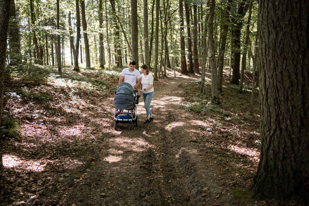 Eltern laufen mit dem Kinderwagen durch den Wald spazieren.