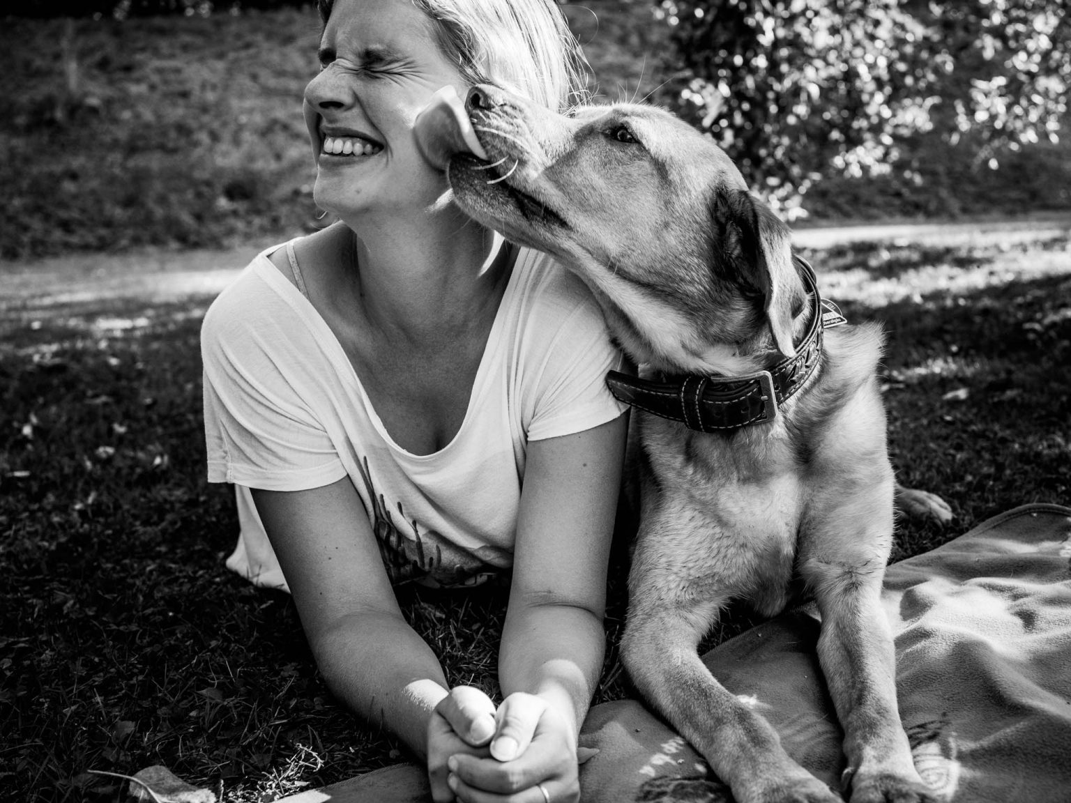 Sandra Neher mit einem Labrador auf dem Bild. Beide liegen auf der Wiese und der Hund schleckt ihr kräftig über das Gesicht.