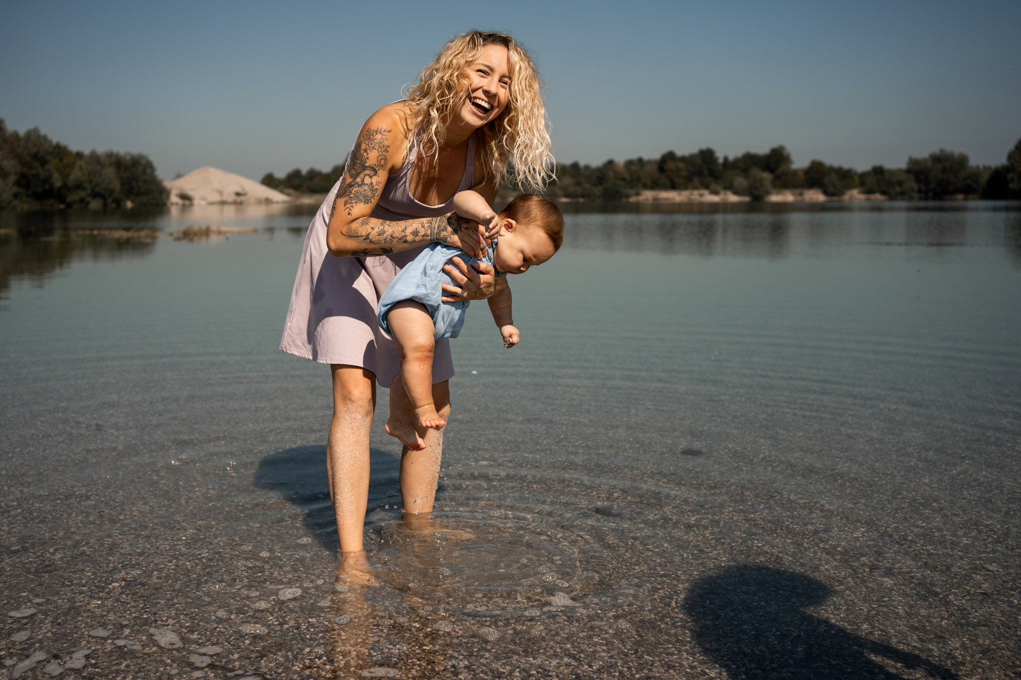 Eine junge Mama steht lachend mit ihrem Baby auf dem Arm im Wasser der Mindelheimer Nordsee.